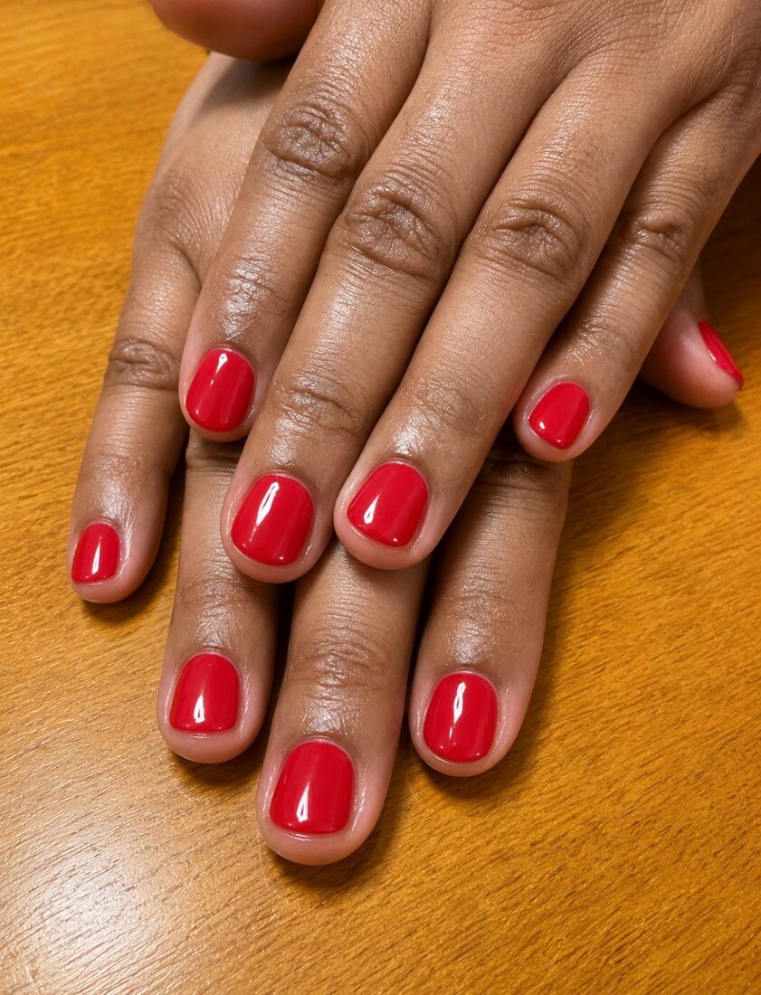 Short natural nails finished in a glossy cherry red by Blush Nail Studio