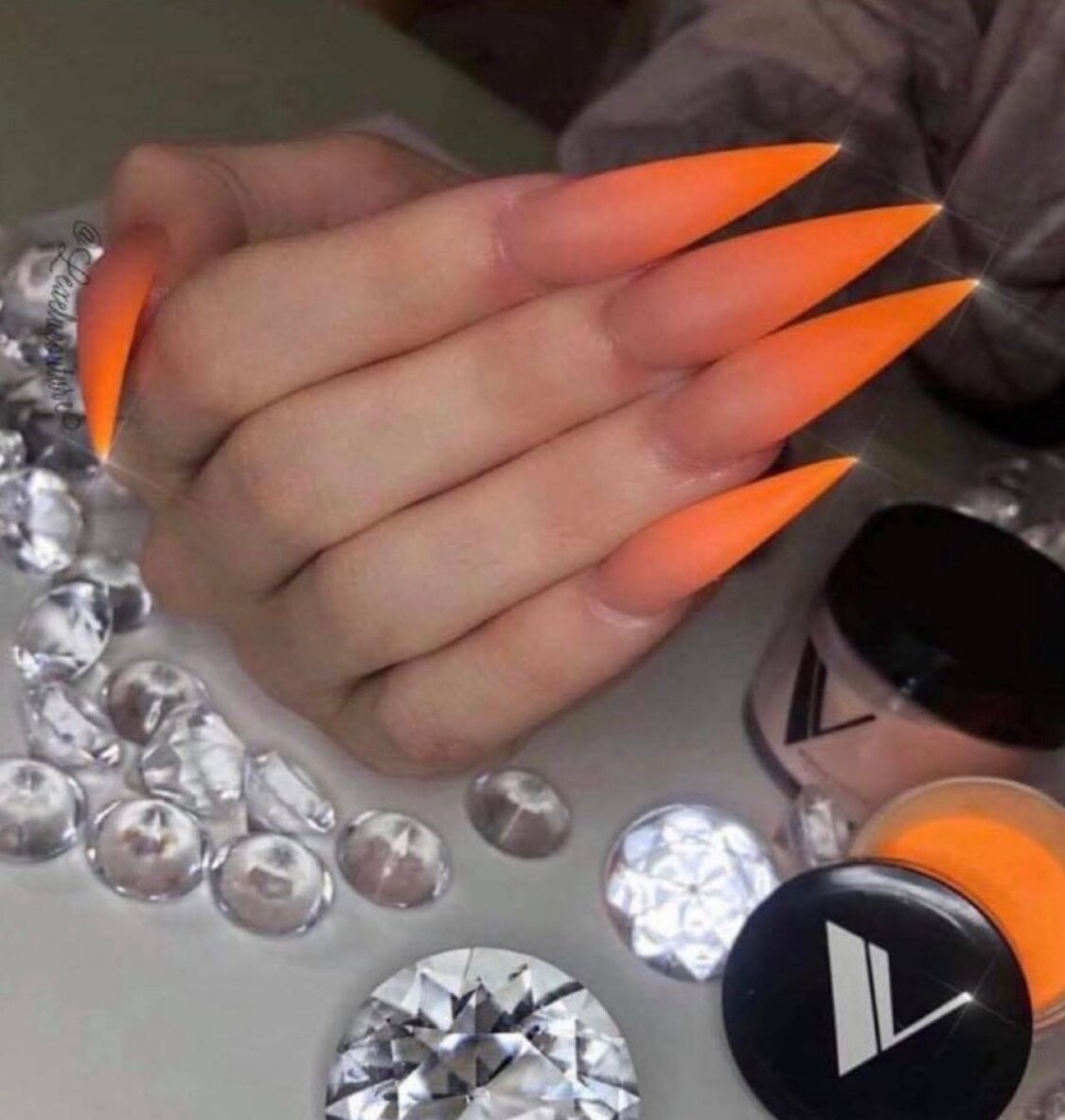 Neon orange stiletto nails surrounded by crystals in the studio